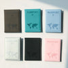 A collection of five slim passport holders in various colors including brown, teal, light blue, black, and pink.