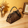 A brown leopard print faux leather handbag with a top handle and crossbody strap resting on a wooden surface.