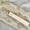 A light beige leather wristlet keychain is displayed on a marbled stone surface.