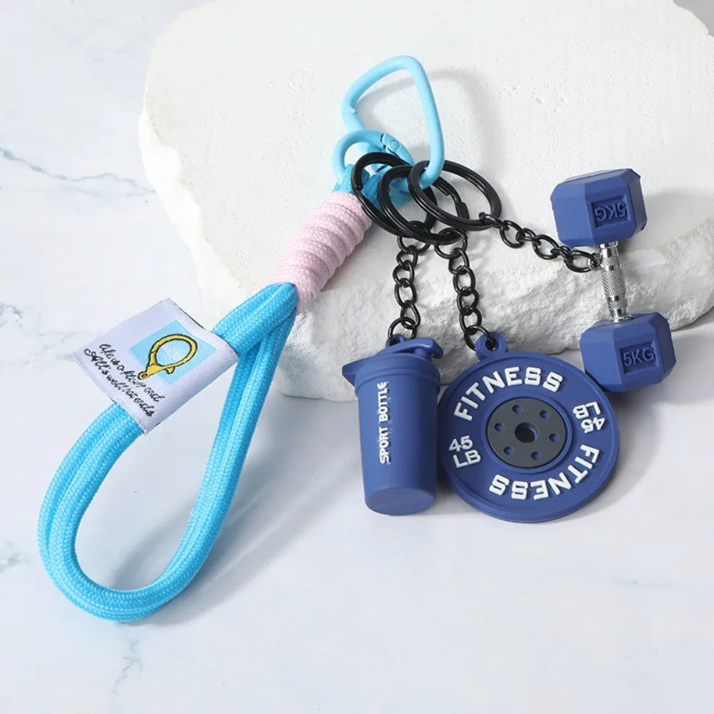 A blue and pink detachable dumbbell keychain charm with a black chain and 5kg weights resting on a white surface.
