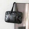 A black leather shoulder bag with a handle is displayed hanging on a wall.