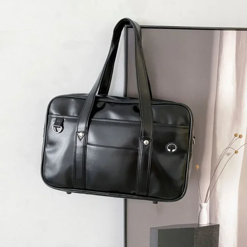 A black leather shoulder bag with a handle is displayed hanging on a wall.