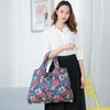 A woman holds a floral patterned canvas tote shopping bag against a white shirt and black skirt.
