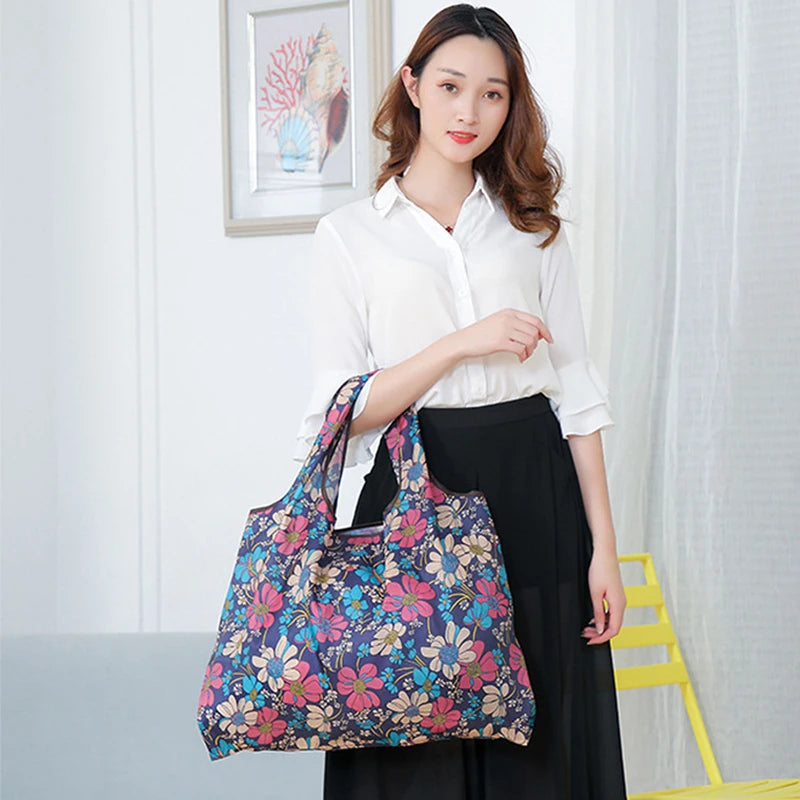 A woman holds a floral patterned canvas tote shopping bag against a white shirt and black skirt.
