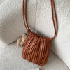 A brown PU leather pleated crossbody bag hanging on a light textured surface next to a small teddy bear.
