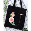 Black canvas tote bag featuring a large pink rose and floral design on the side.