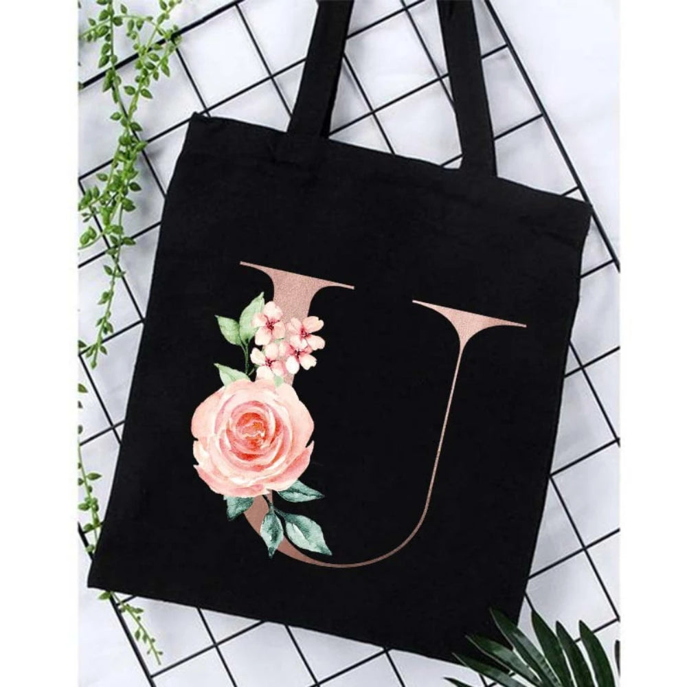 Black canvas tote bag featuring a large pink rose and floral design on the side.