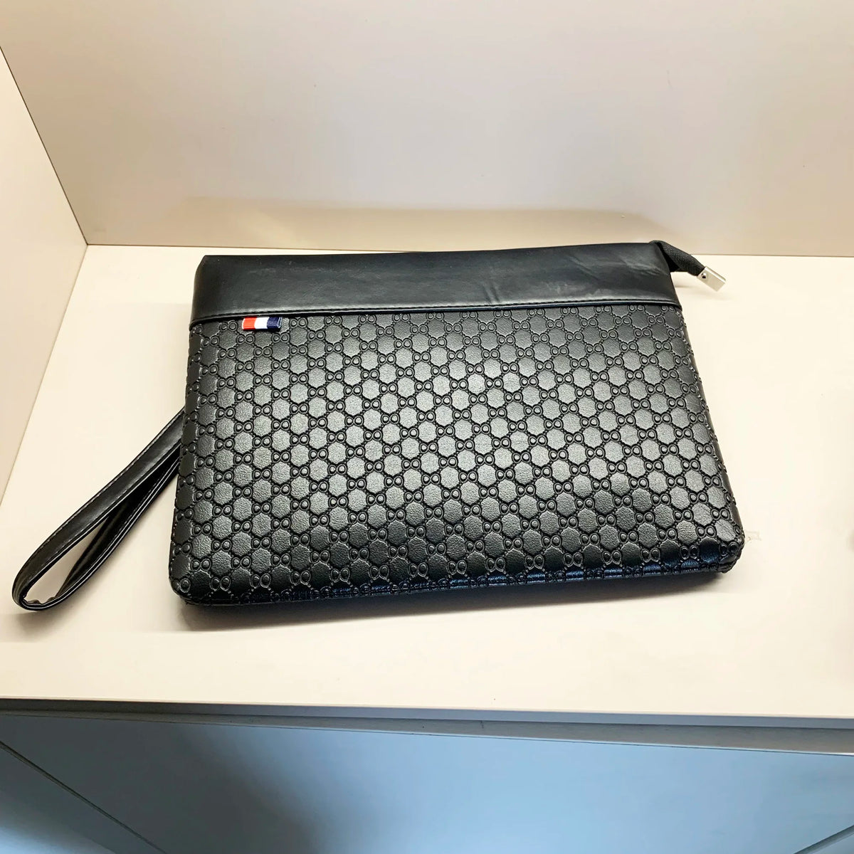 A black quilted PU leather clutch bag with a flap and a small leather strap resting on a white surface.
