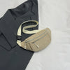 A beige corduroy crossbody waist bag with a light strap resting on a dark gray blazer.