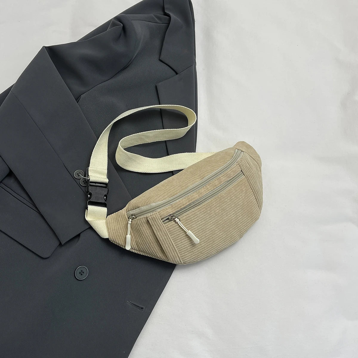 A beige corduroy crossbody waist bag with a light strap resting on a dark gray blazer.