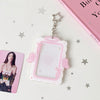 A clear acrylic photocard holder with pink decorative frame and angel wings, suspended by a silver chain.