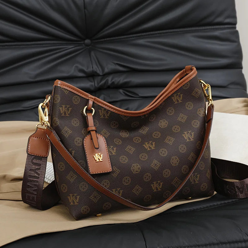 A brown leather crossbody tote bag with a monogram pattern resting on a dark surface.