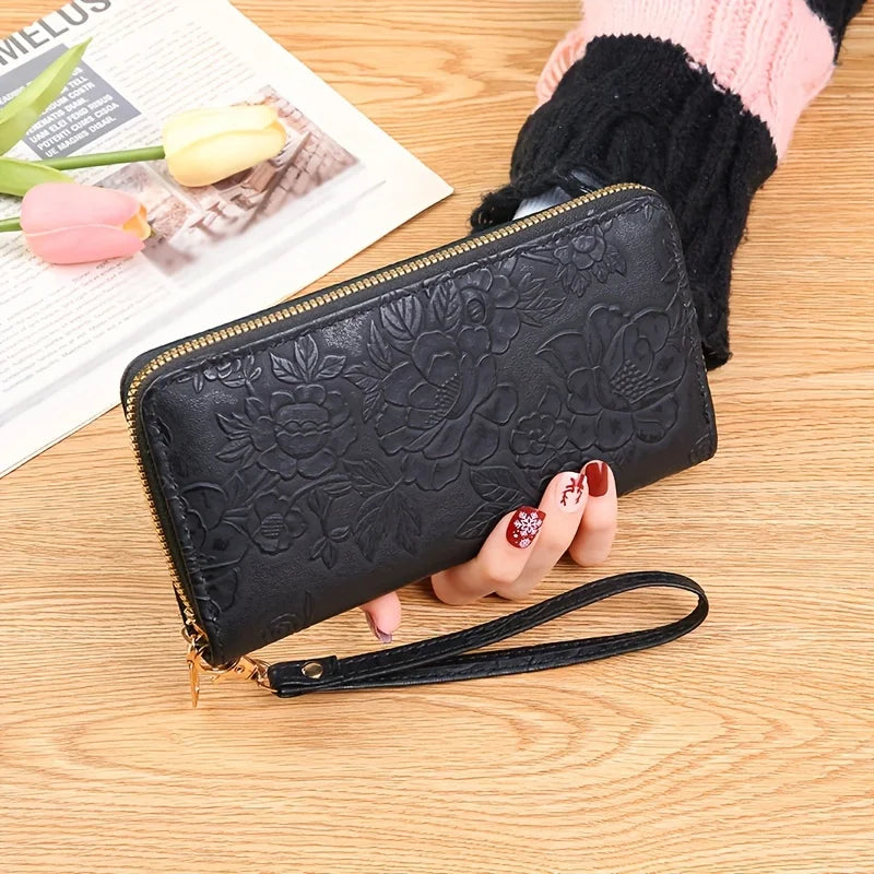 Cartera de tarjeta de cuero PU floral negro con cremallera y correa dorada sobre una superficie de madera.