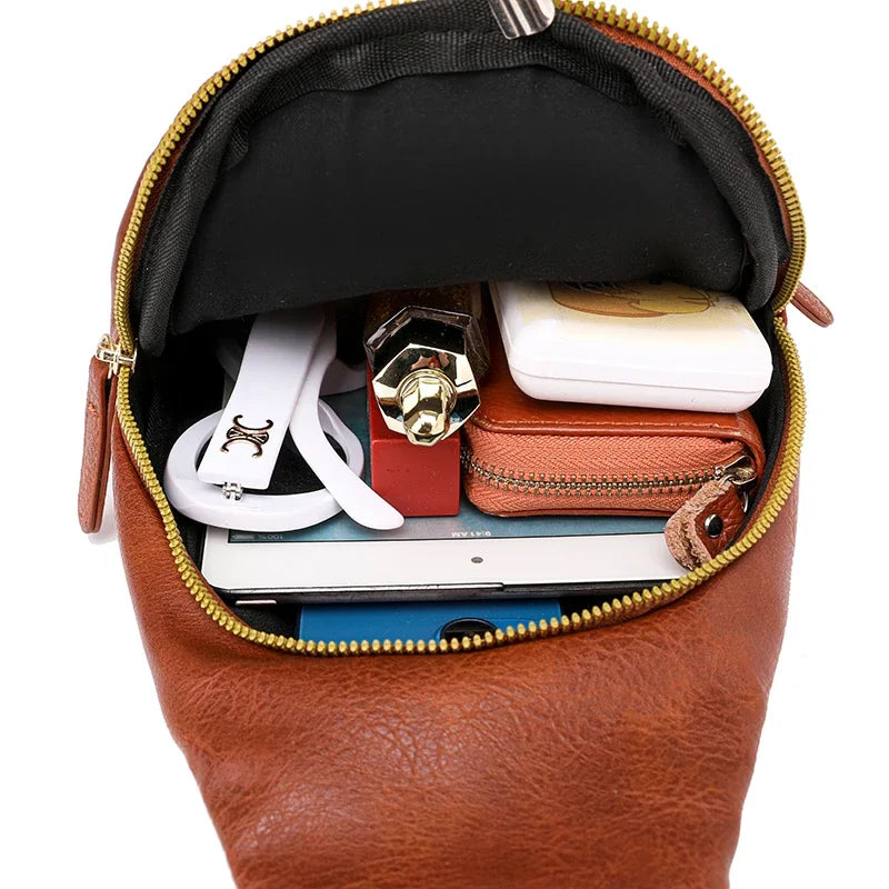 A brown PU leather crossbody sling bag is shown open, revealing a lined interior with various small accessories.