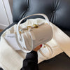 A white leather shoulder bag with gold hardware resting on a cream blanket on a dark leather surface.