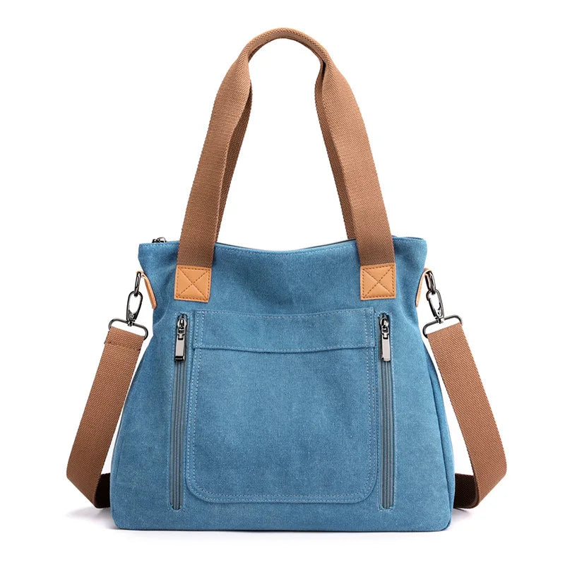 A medium blue canvas tote bag with tan leather straps and zipper details.