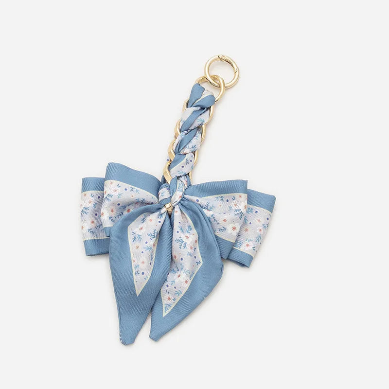 A light blue fabric bow bag chain strap extension with a gold-colored ring.