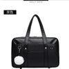 Black leather shoulder bag with a white pom-pom detail shown from an angle.