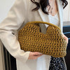 A woman holds a woven straw tote handbag with a light brown color against a white blazer.
