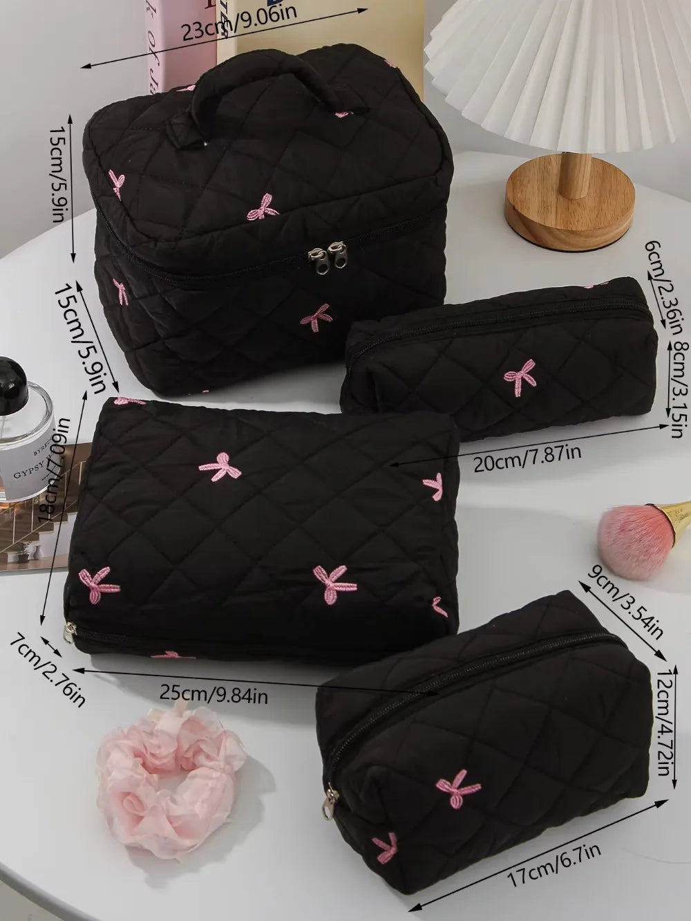 A collection of black quilted cosmetic bags with pink bows displayed on a white surface.