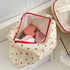 A cream quilted makeup bag with a red zipper and pink lining, featuring a pattern of small red hearts.
