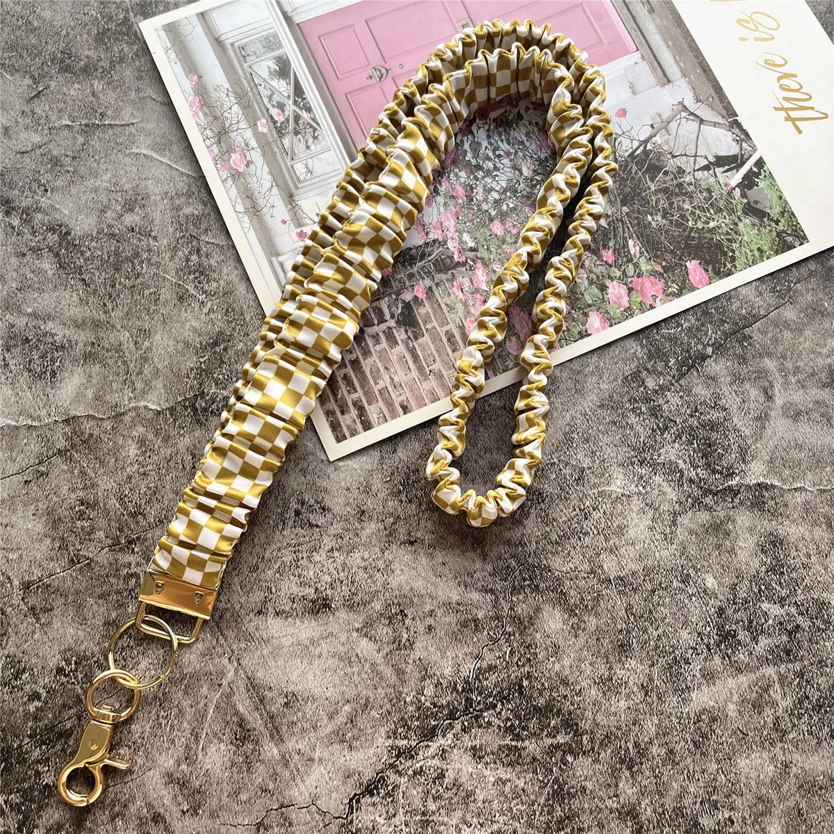 Gold-cremiges kariertes Stoff-Lanyard mit Schlüsselring auf texturierter grauer Oberfläche