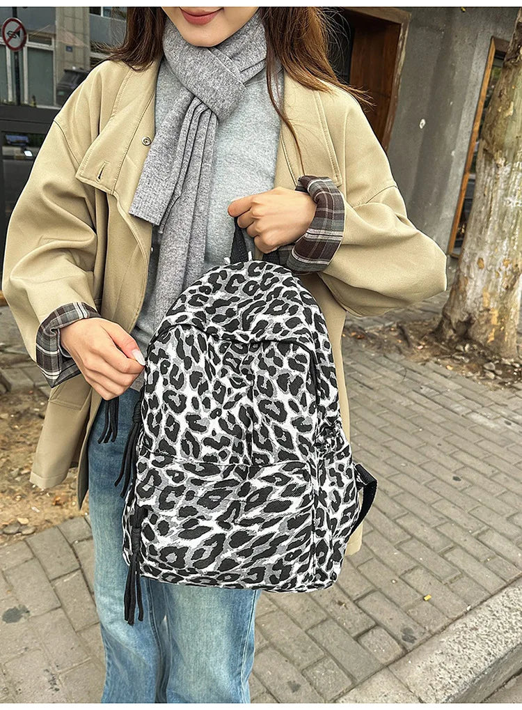 A woman wearing a beige coat and gray sweater carries a leopard print canvas backpack.