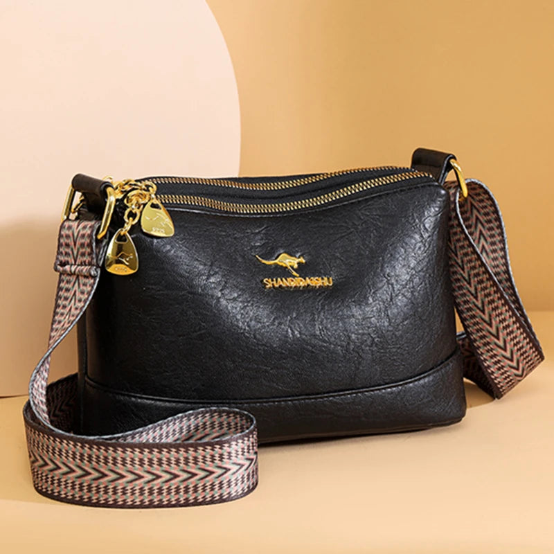 Black luxury PU leather crossbody handbag with gold hardware and patterned strap on a beige background.