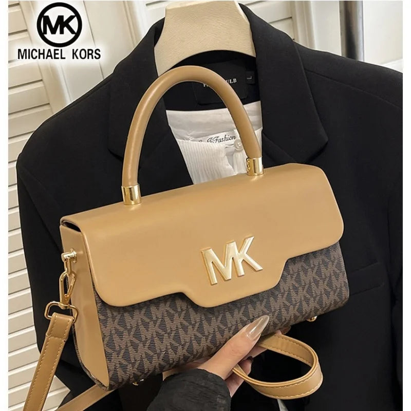A tan Michael Kors letter square crossbody bag with a brown patterned fabric and gold hardware being held by a person.