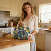 A woman stands in a kitchen holding a blue and yellow thermal storage bag.