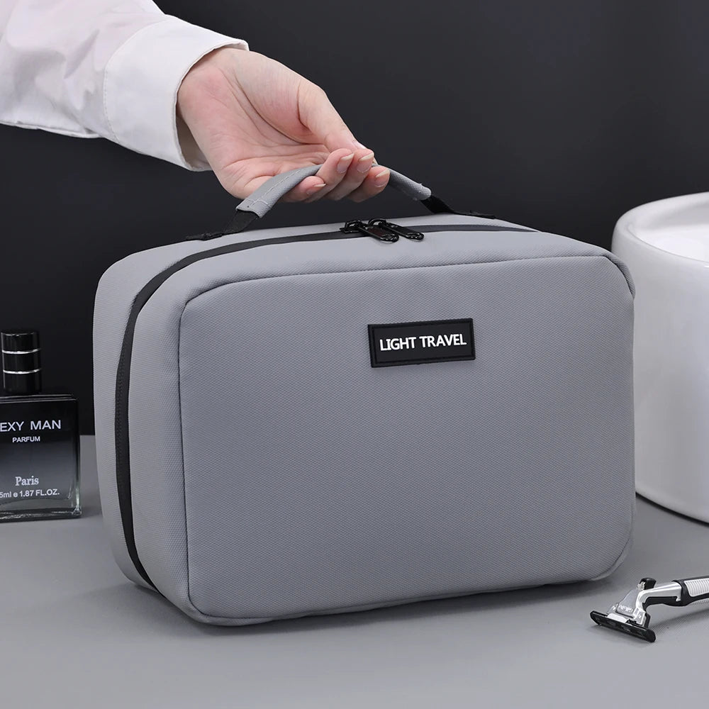 A hand is opening a gray portable waterproof travel toiletry bag labeled Light Travel on a gray surface.