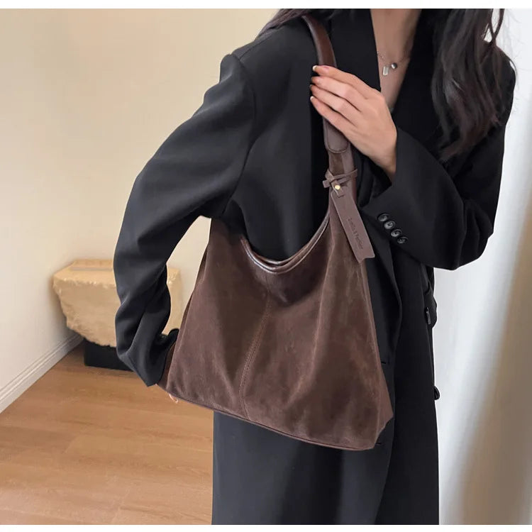 A woman holds a dark brown suede slouchy shoulder bag against a black coat.