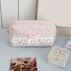 A pink quilted cosmetic storage pouch with white lace trim and a pink bow, next to a white cosmetic jar.