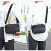 A man wearing a white shirt and dark pants carries a black PU leather shoulder clutch bag on his back.