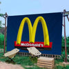 A large blue banner featuring the yellow McDonald's arches logo outdoors with surrounding greenery.
