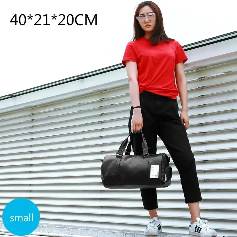 Eine Frau in rotop Shirt und schwarzen Hosen hält eine schwarze PU-Leder-Sporttasche vor einer silbernen Wellblechwand.