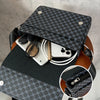 A black patterned flap crossbody bag is shown resting on a wooden stand, with a smartphone and sunglasses inside.