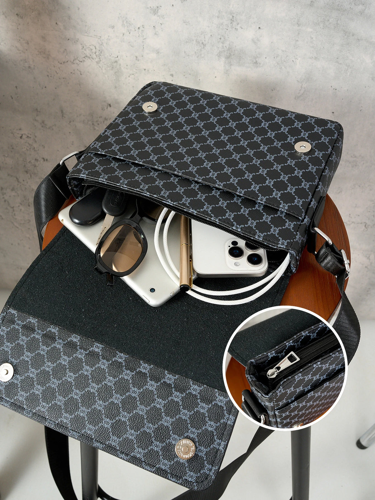 A black patterned flap crossbody bag is shown resting on a wooden stand, with a smartphone and sunglasses inside.