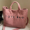 Un sac fourre-tout côtelé rose avec des lettres noires, debout.