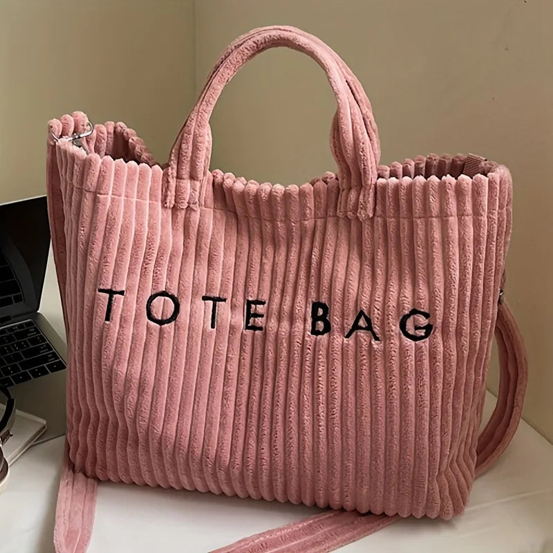A pink ribbed canvas tote bag with black lettering is shown standing upright.