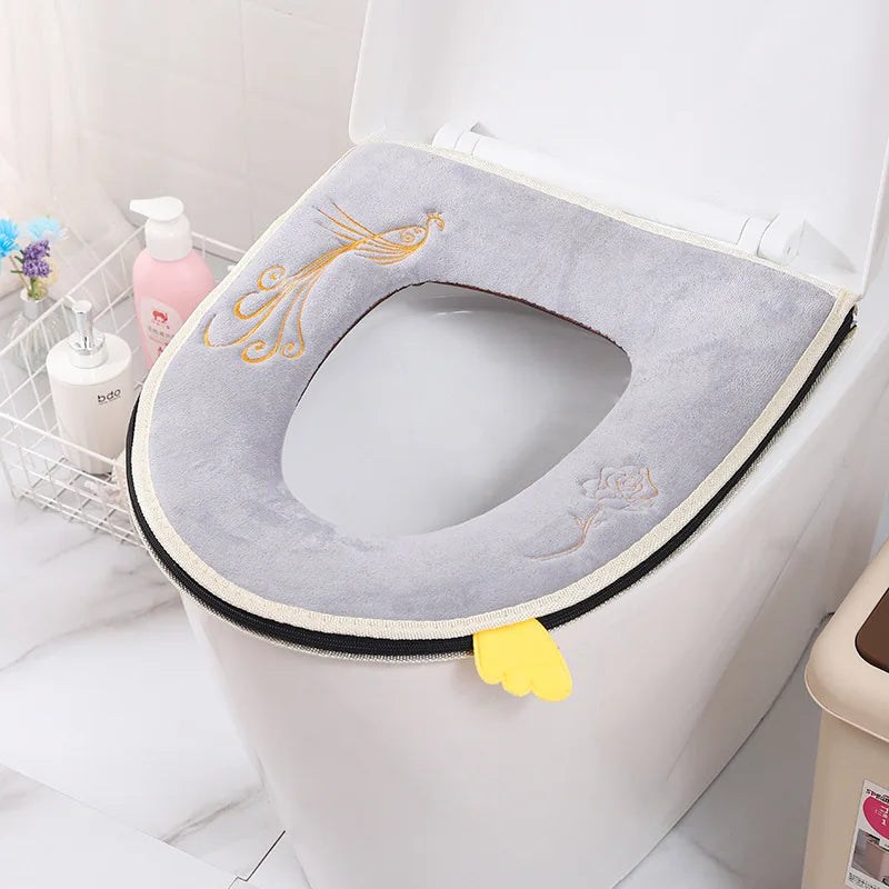 A plush gray waterproof toilet seat cover with an orange decorative design and a yellow grip is shown inside a white toilet b