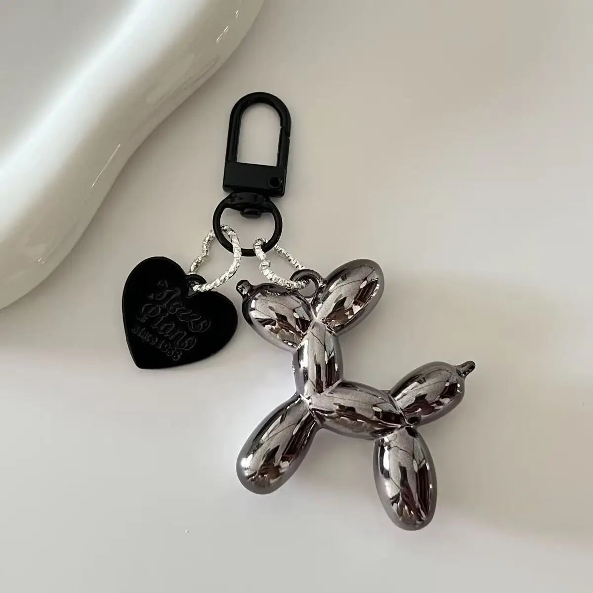 A silver balloon dog keychain charm with a black heart tag and metal keyring.