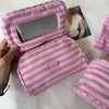 A pink striped makeup bag with a flip-top mirror is shown being held by a hand, next to another matching pouch.
