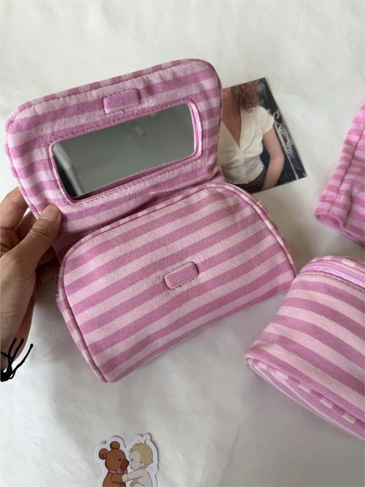 A pink striped makeup bag with a flip-top mirror is shown being held by a hand, next to another matching pouch.