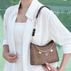 A woman holds a brown mini strap bag with an extension chain and leather accents against a white shirt.