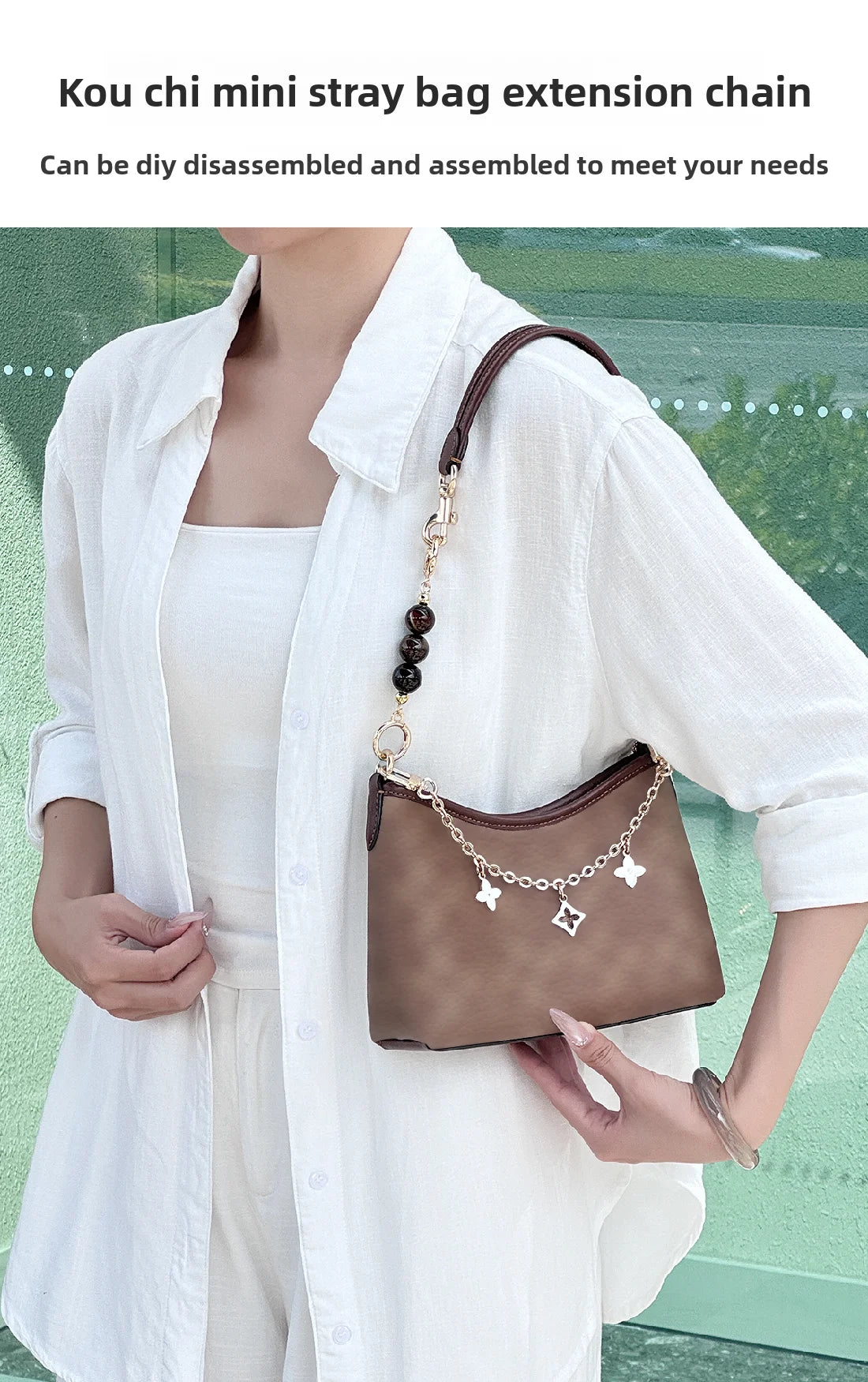 A woman holds a brown mini strap bag with an extension chain and leather accents against a white shirt.