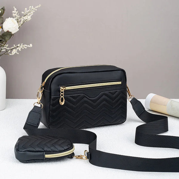 Black quilted pattern crossbody bag with gold hardware resting on a white surface.