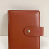 A brown leather ring binder notebook with a stitched cover and silver clasp.