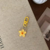 A yellow resin flower keychain with a gold split ring attached, resting on a beige fabric surface.