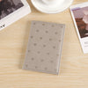 A light gray leather passport cover with a subtle pattern of small heart prints resting on a wooden surface.